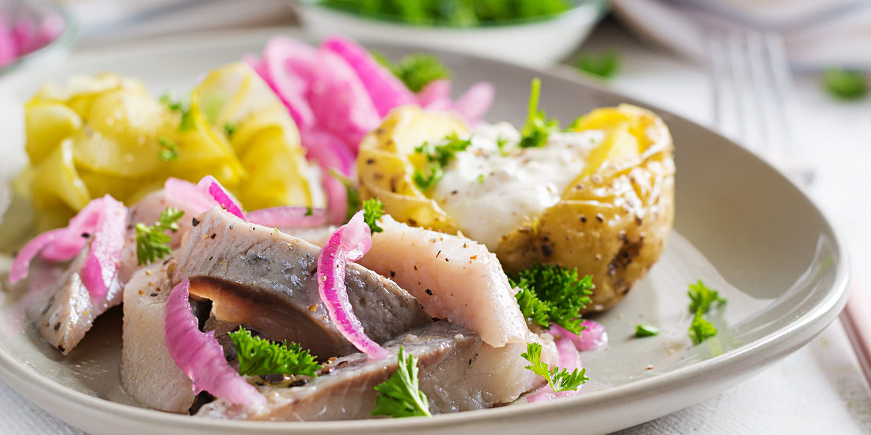Herring with baked potato, onions and pickled cucumber on a plate. Traditional cuisine.